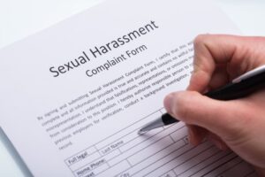 Close-up Of A Human Hand Filling Sexual Harassment Complaint Form With Pen